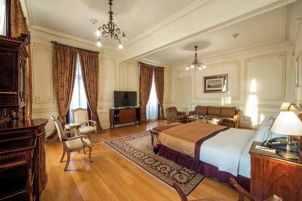 A hotel room with a large bed, a television, a desk with a lamp, and a sofa.