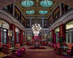 A grand lobby with a chandelier, red upholstered furniture, and ornate ceiling details.