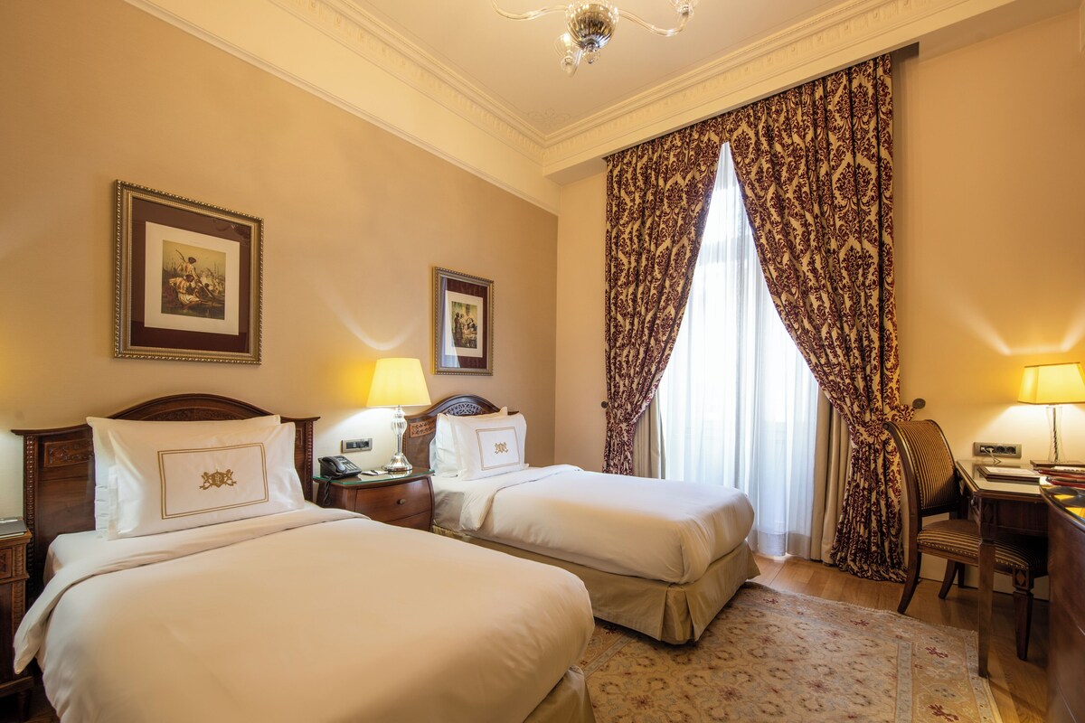 A hotel room with two beds, a desk, a chair, a telephone, and a window with curtains.