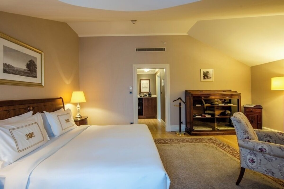 A hotel room with a large bed, a desk, a chair, a bookshelf, and a framed picture on the wall.