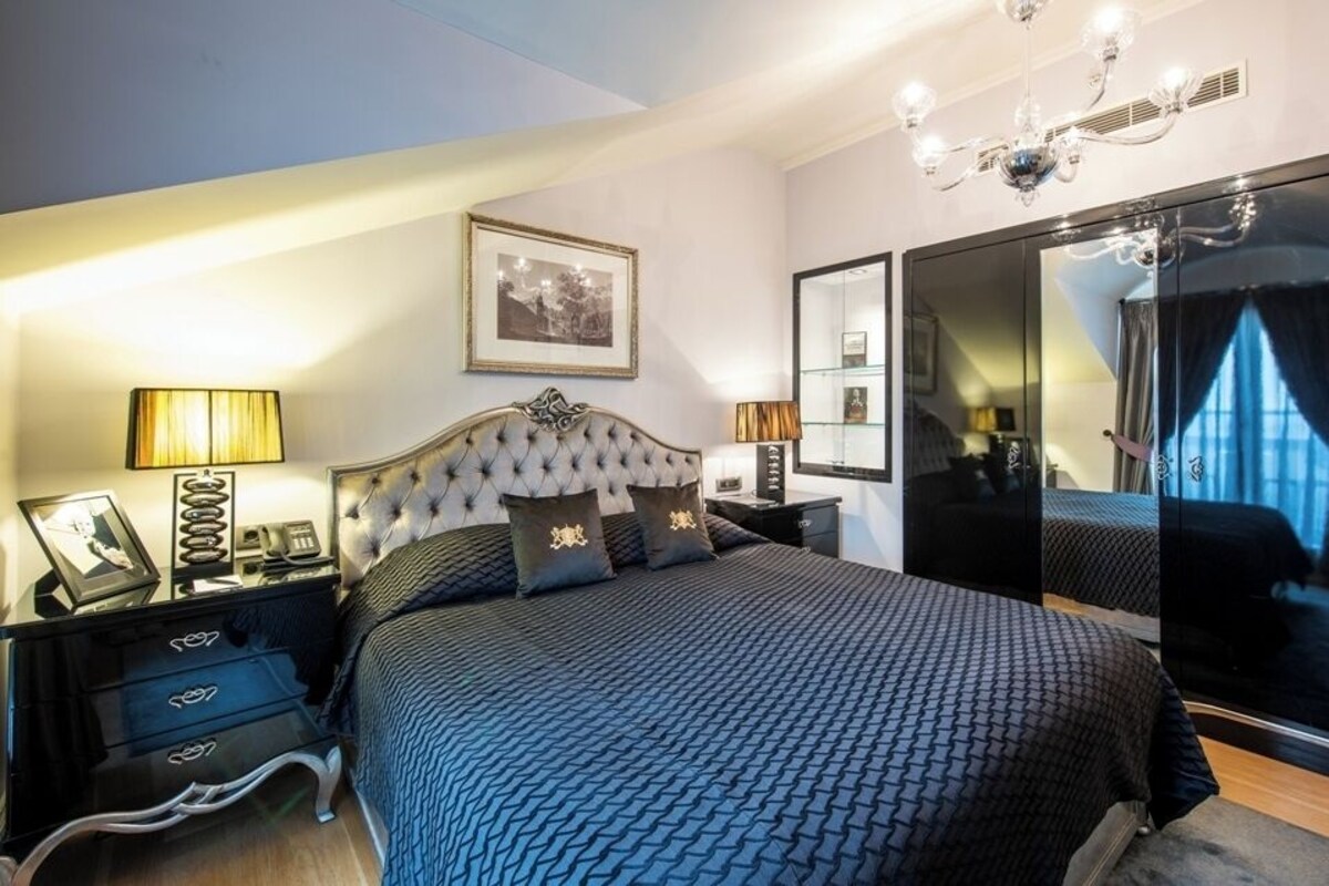A bedroom with a large bed, a dresser, a nightstand, a mirror, and a chandelier.