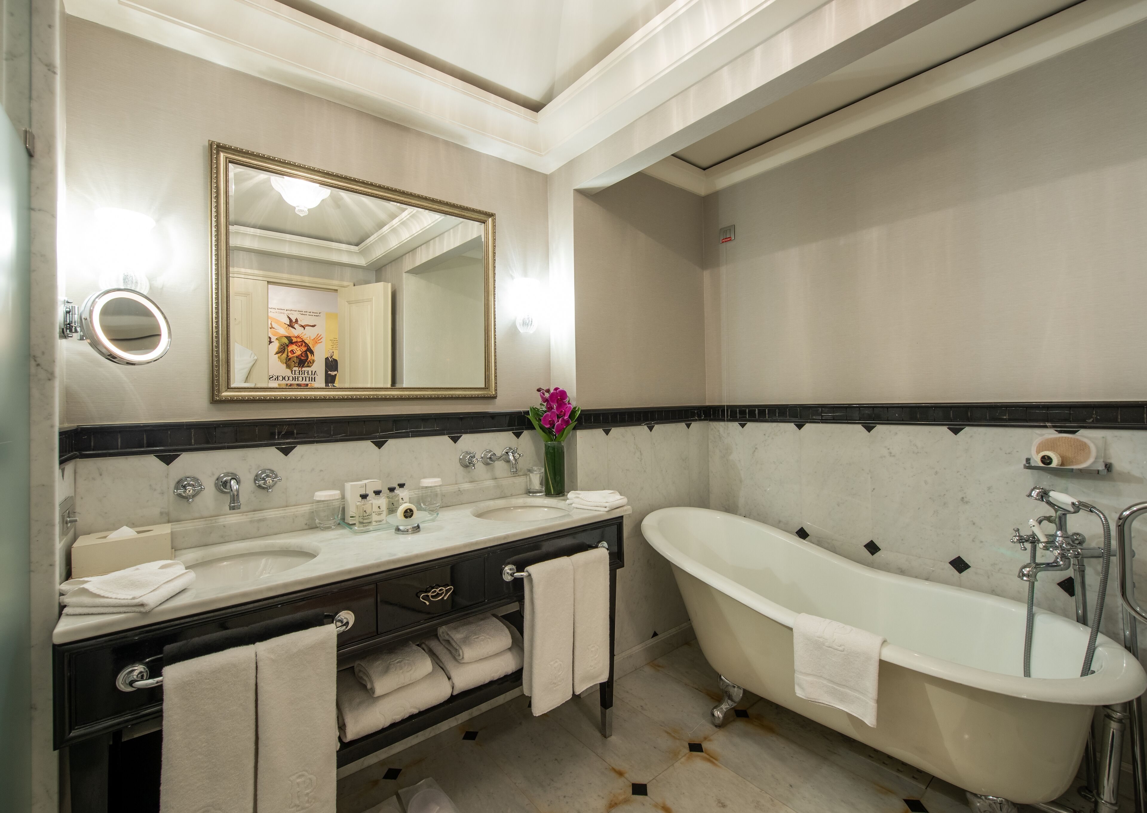 A bathroom with two sinks, a large mirror, a bathtub, and a vase with flowers.