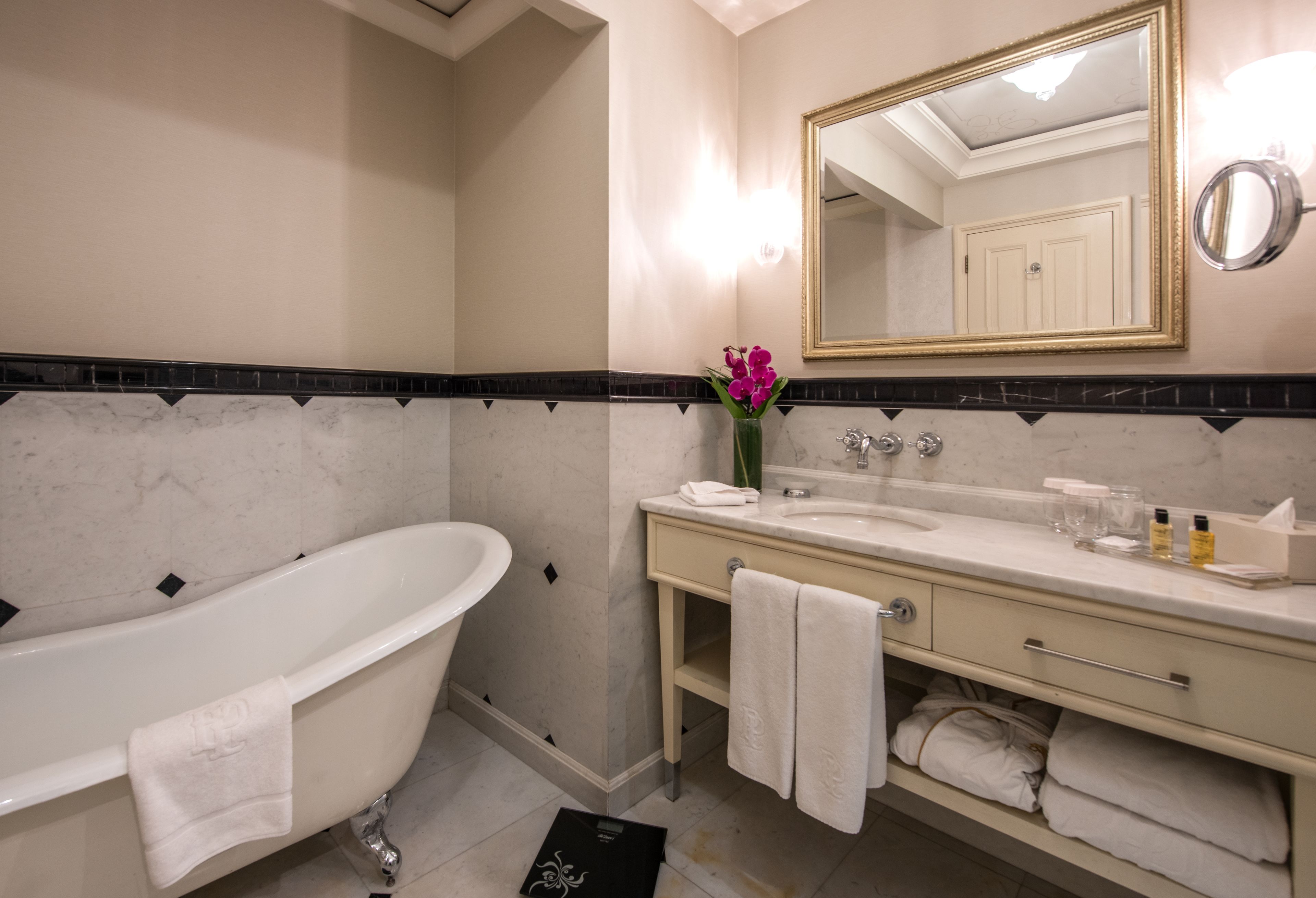 A bathroom with a freestanding bathtub, a vanity with a mirror, and a vase with flowers.