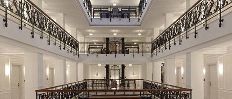 A grand interior with a central open space, ornate black railings, and a glass ceiling.