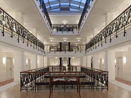 A grand interior with a central open space, ornate black railings, and a glass ceiling.
