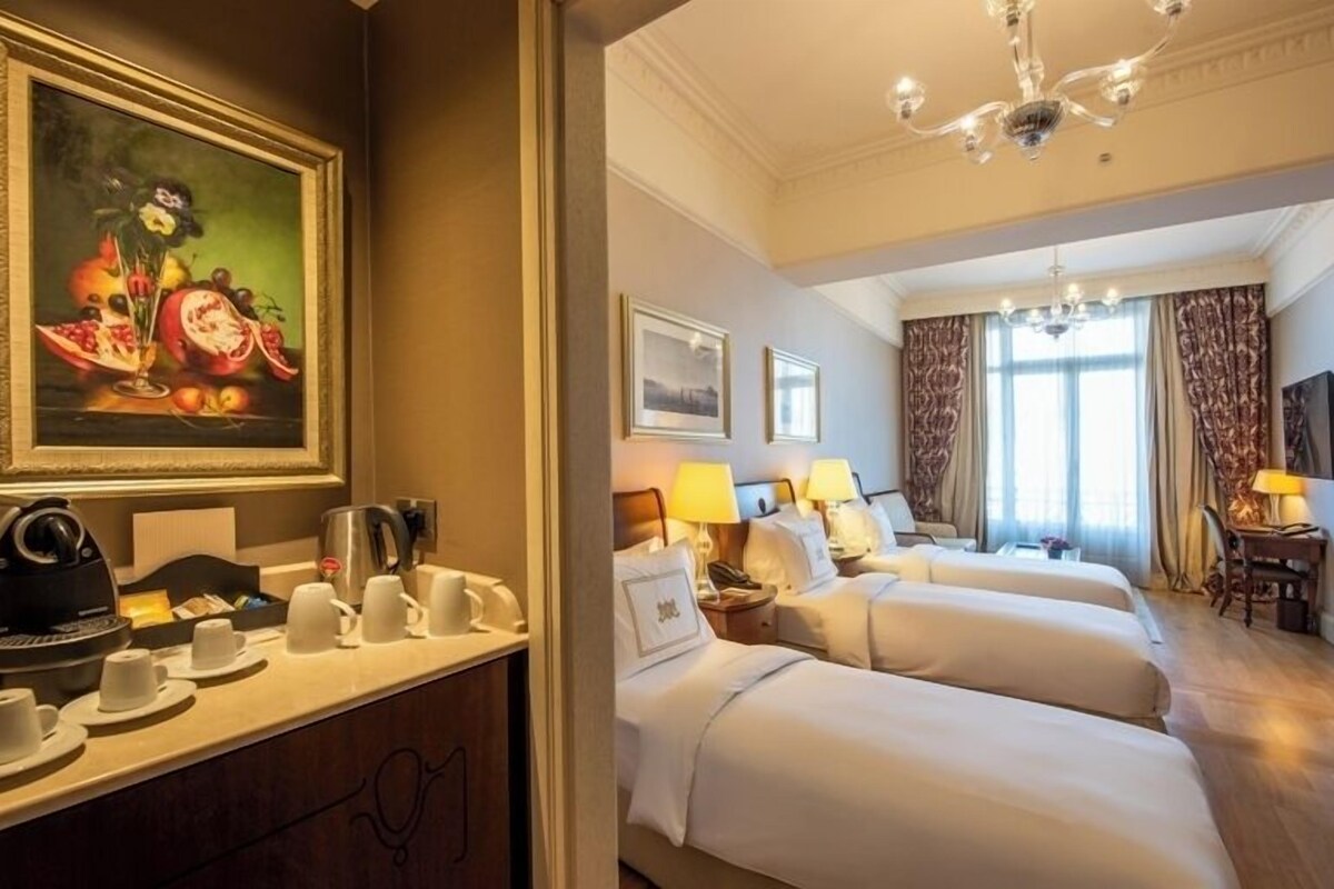A hotel room with a bed, bedside tables, lamps, a painting, and a coffee station.