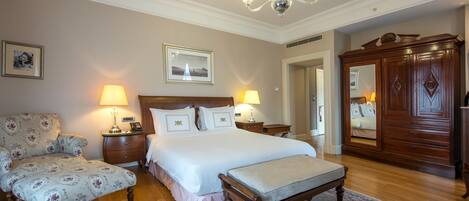 A bedroom with a large bed, two bedside lamps, a wooden wardrobe, a chair, and a small table.