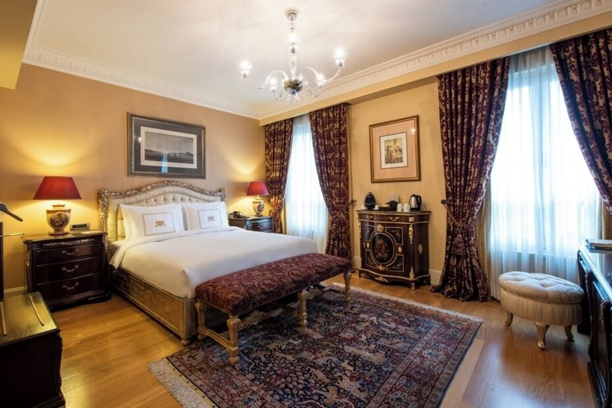 A bedroom with a large bed, a bench, a nightstand, a dresser, a mirror, and a chandelier.