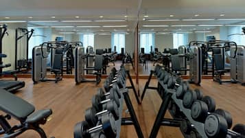 Ein Fitnessstudio mit verschiedenen Trainingsgeräten, darunter Laufbänder, Kraftgeräte und Kurzhanteln.