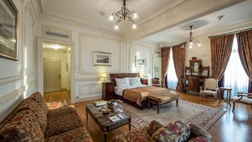 A spacious bedroom with a large bed, a sitting area with sofas, a wooden desk, and a chandelier.