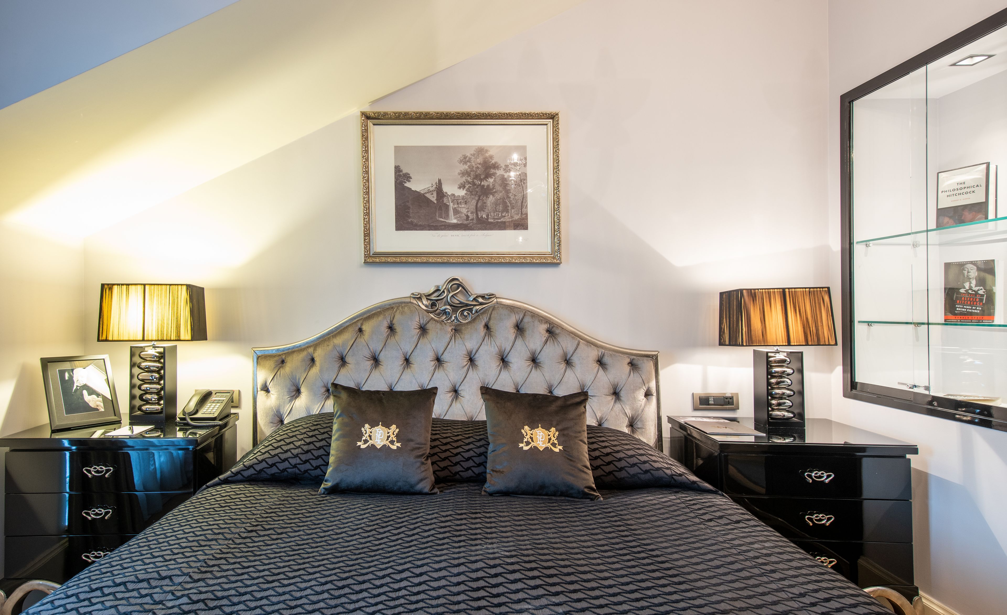 A bedroom with a tufted headboard, two bedside tables with lamps, a framed picture on the wall, and a large mirror.