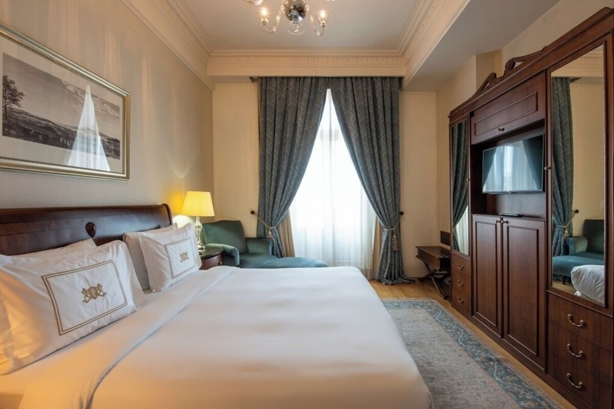 A hotel room with a large bed, a TV, a desk, and a chair.