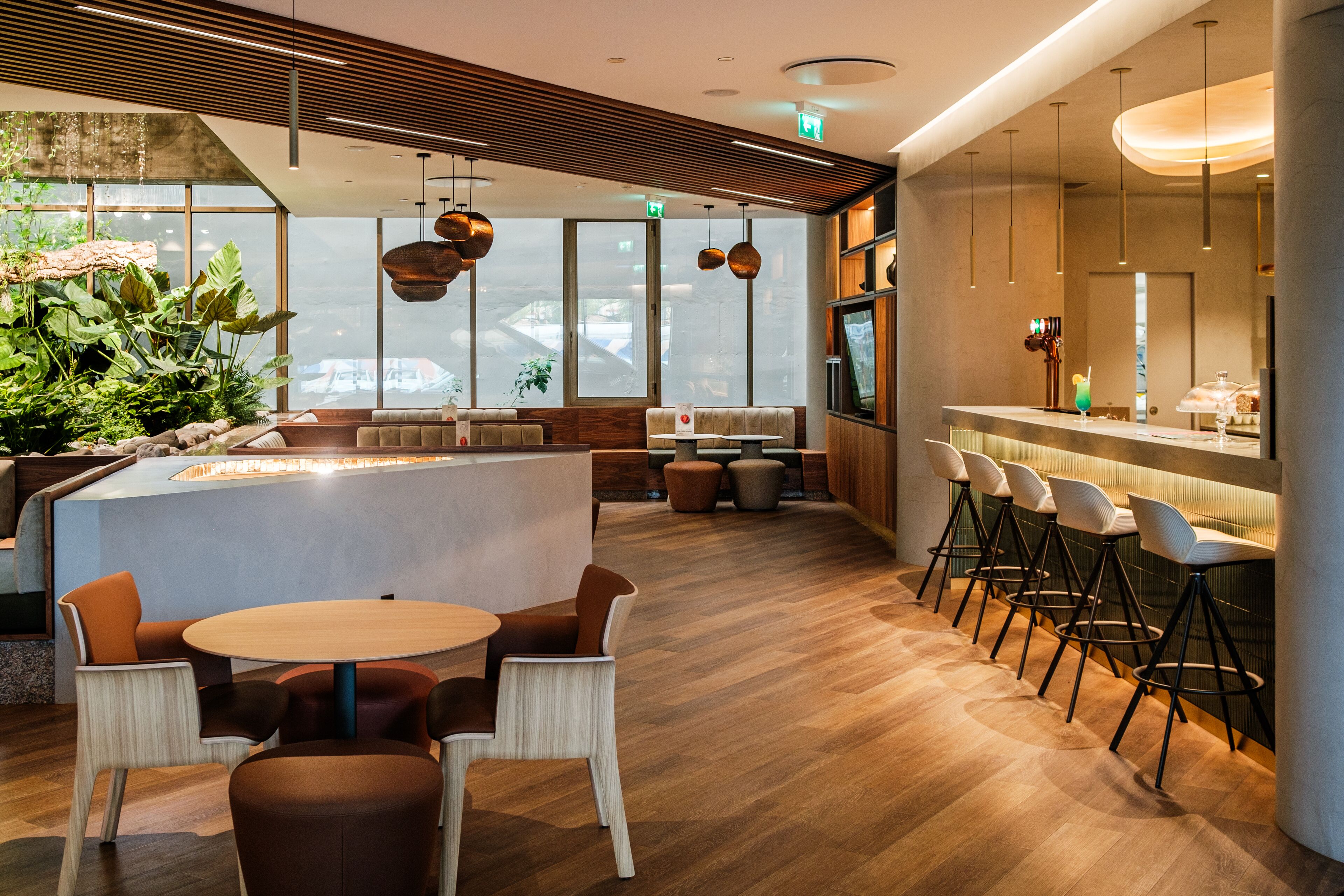 Un bar moderno con suelo de madera, taburetes y una zona de estar con mesas redondas y sillas.