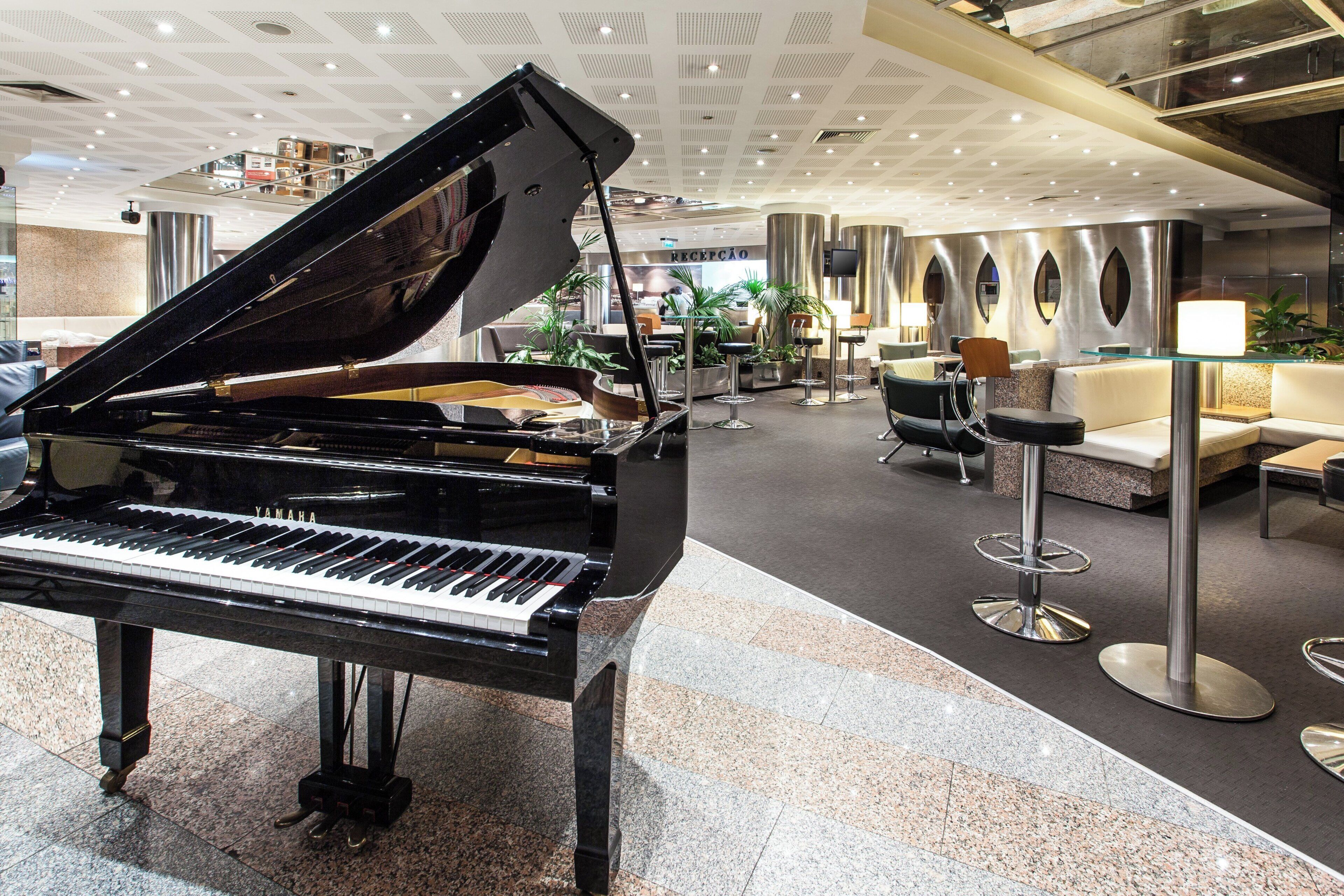 Un magnifique piano à queue trône dans un hall spacieux, agrémenté d’un décor moderne, de coins salon et d’un comptoir d’accueil.