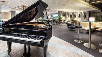 Un magnifique piano à queue trône dans un hall spacieux, agrémenté d’un décor moderne, de coins salon et d’un comptoir d’accueil.