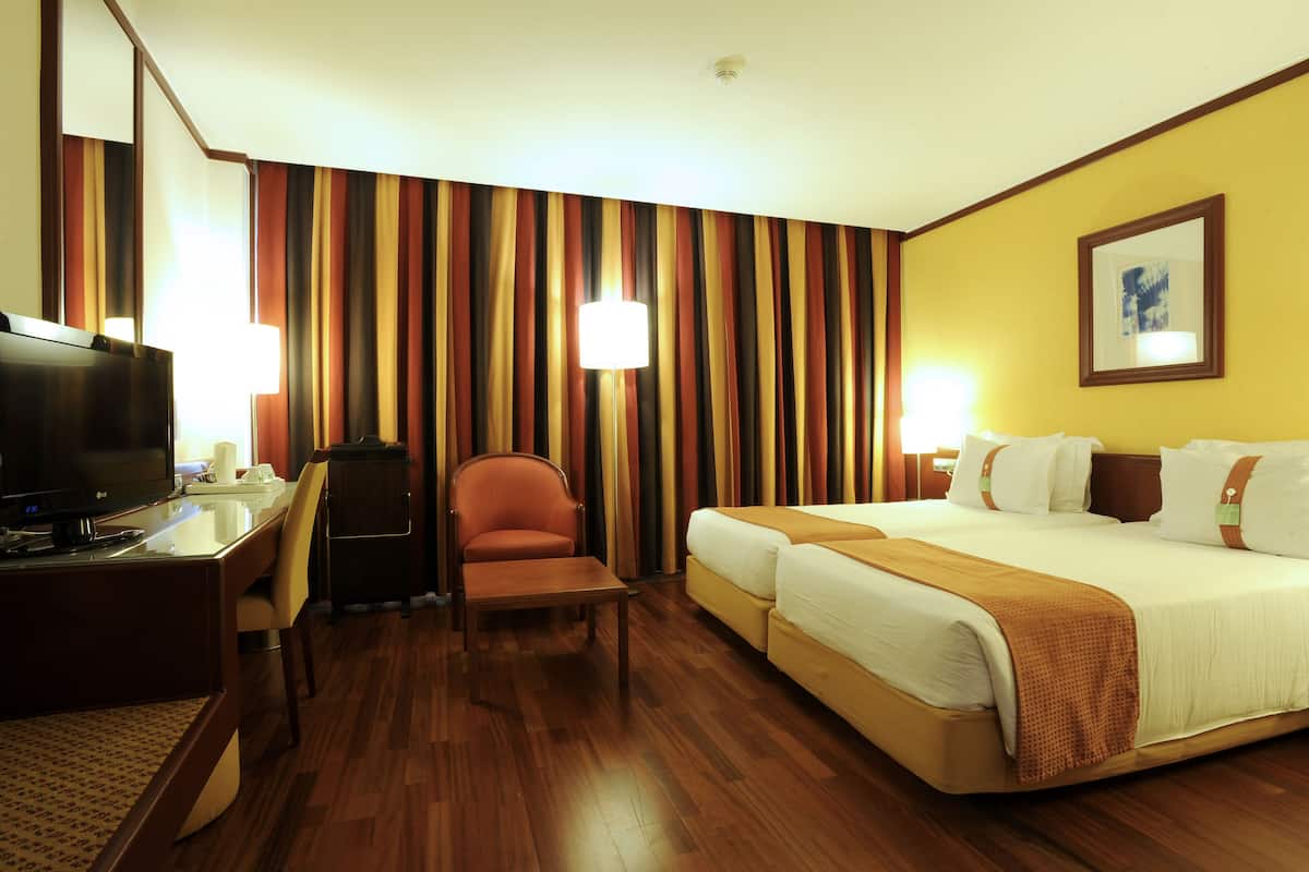 A hotel room with a bed, a desk with a TV, a chair, and a lamp.