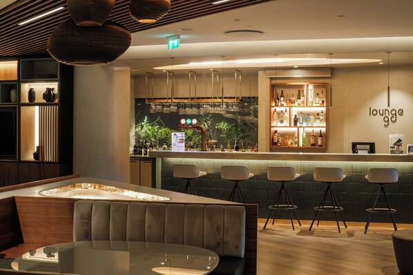 A modern lounge area with a bar, seating, and a decorative wall. - Holiday Inn Lisbon Continental by IHG (Lisbon)