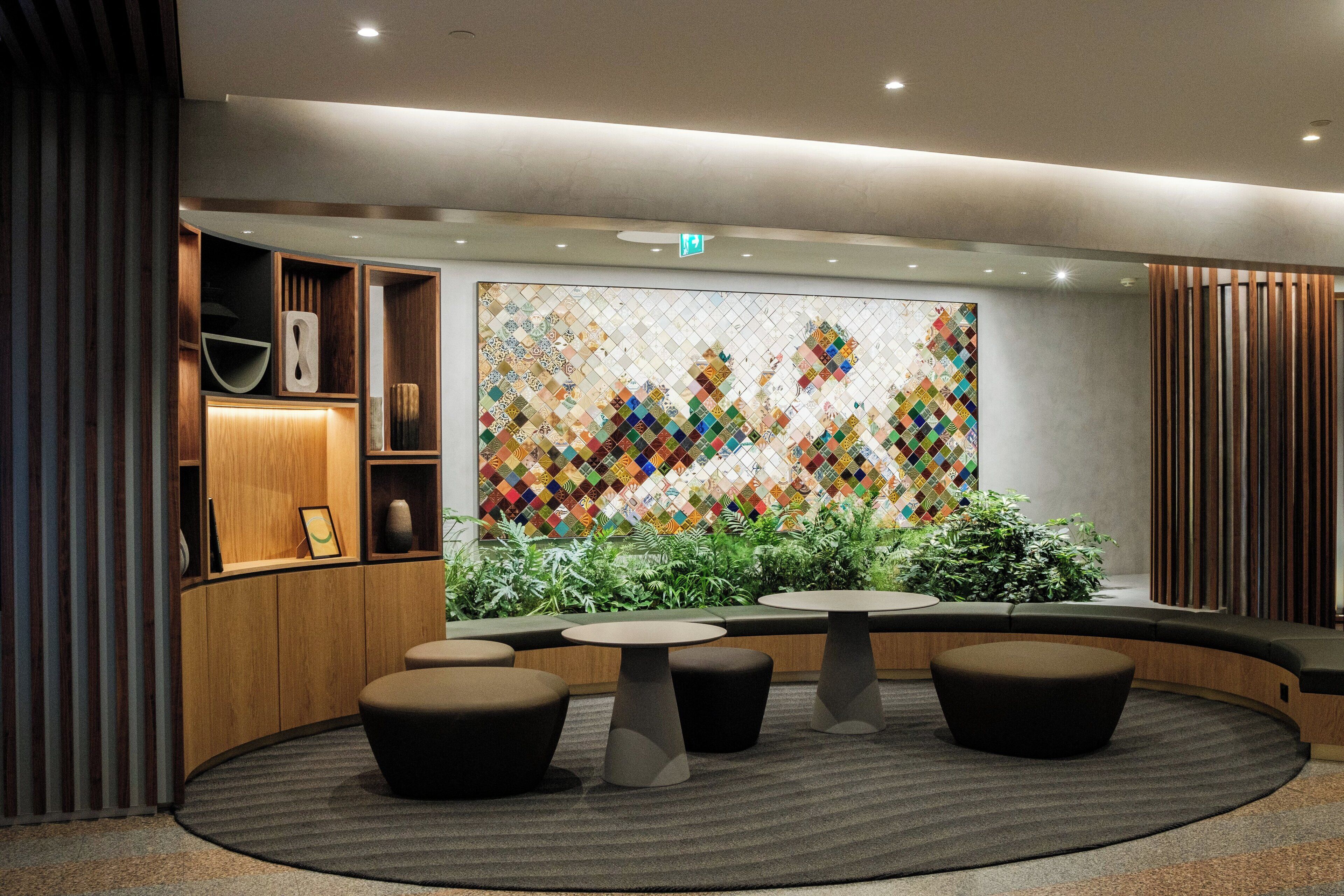A modern lobby with a large colorful mosaic wall, wooden shelving, and round seating areas.