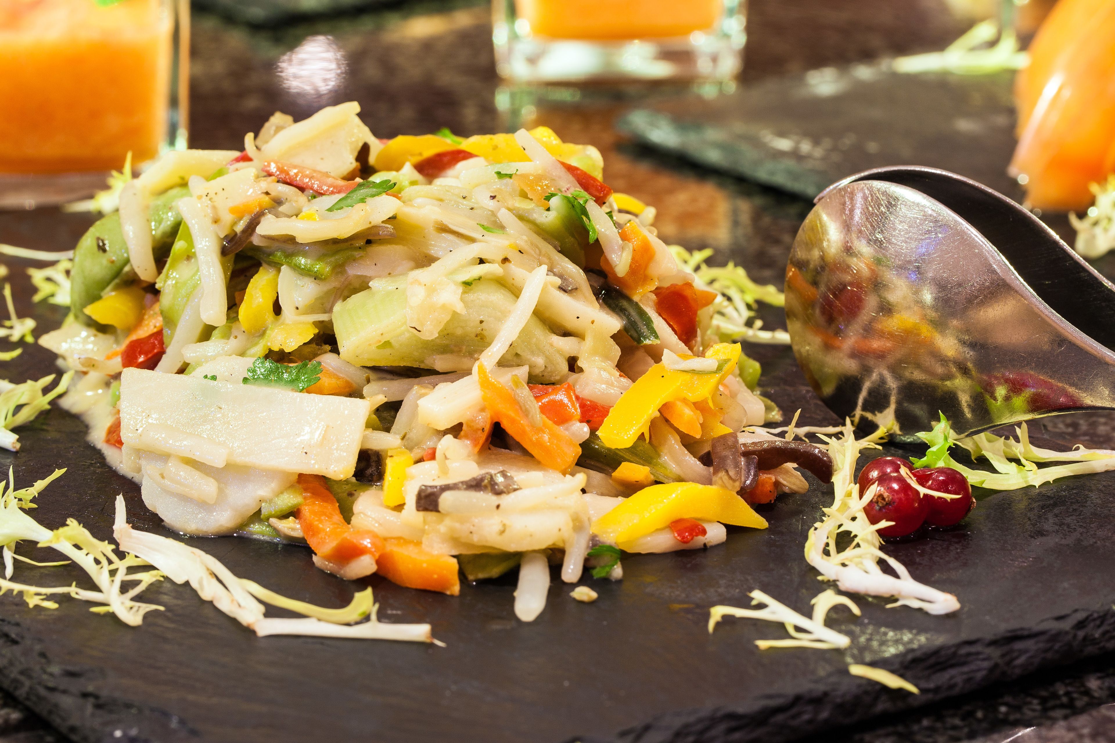 Ensalada de vegetales coloridos sobre un plato de pizarra oscura con una cuchara.