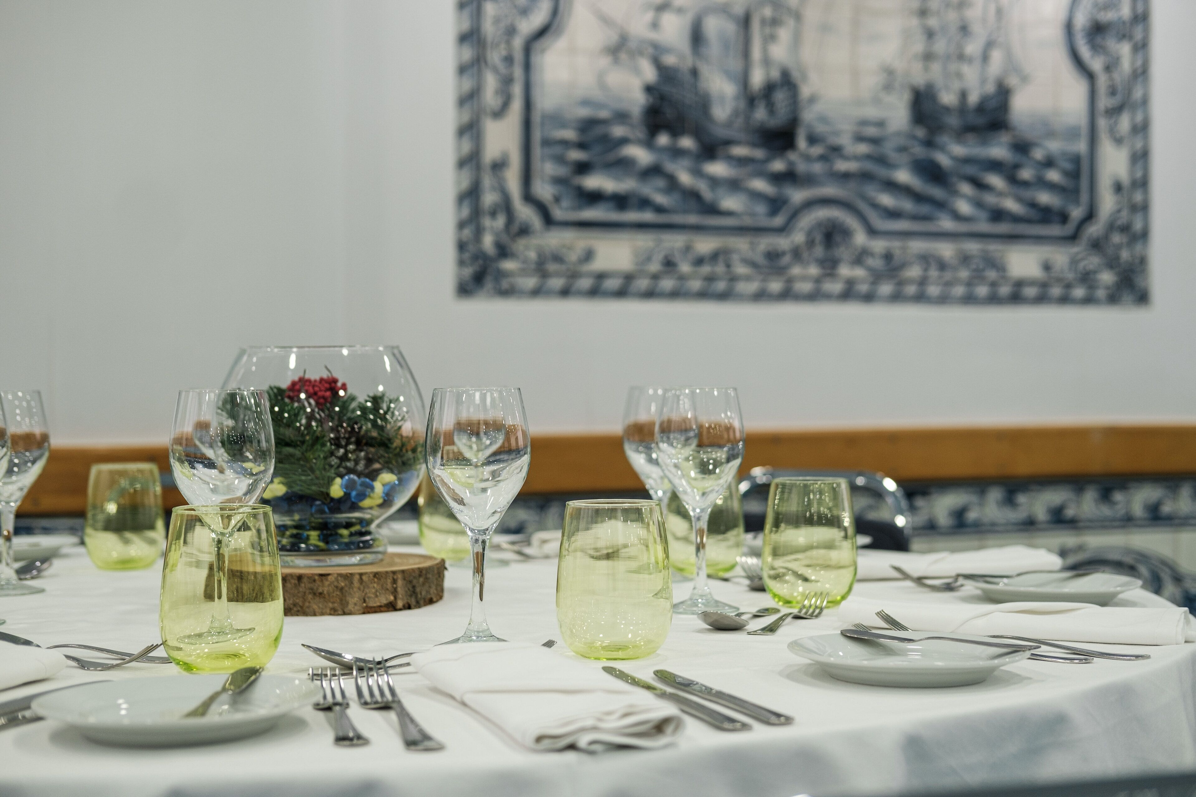 A dining table set with wine glasses, plates, and cutlery, with a decorative centerpiece and a blue and white patterned wall behind.