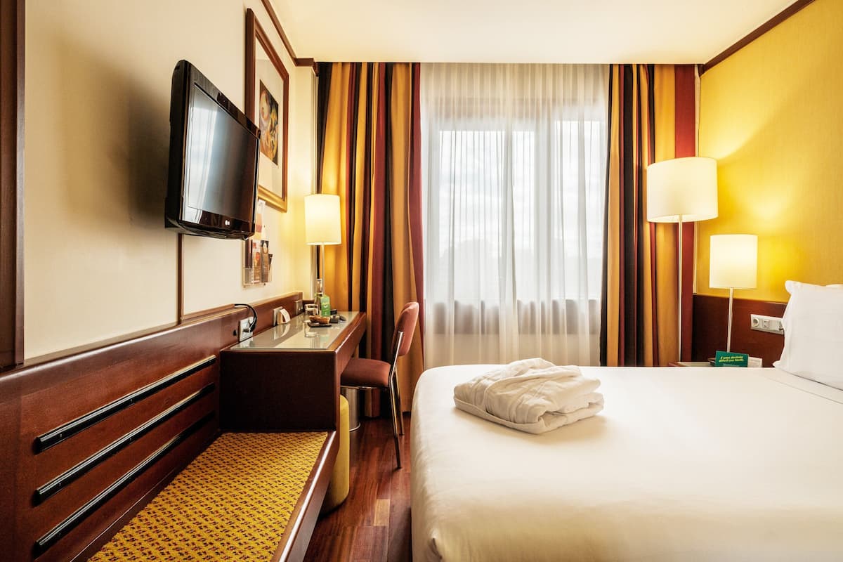A hotel room with a bed, a desk, a chair, a television, and a window with curtains.