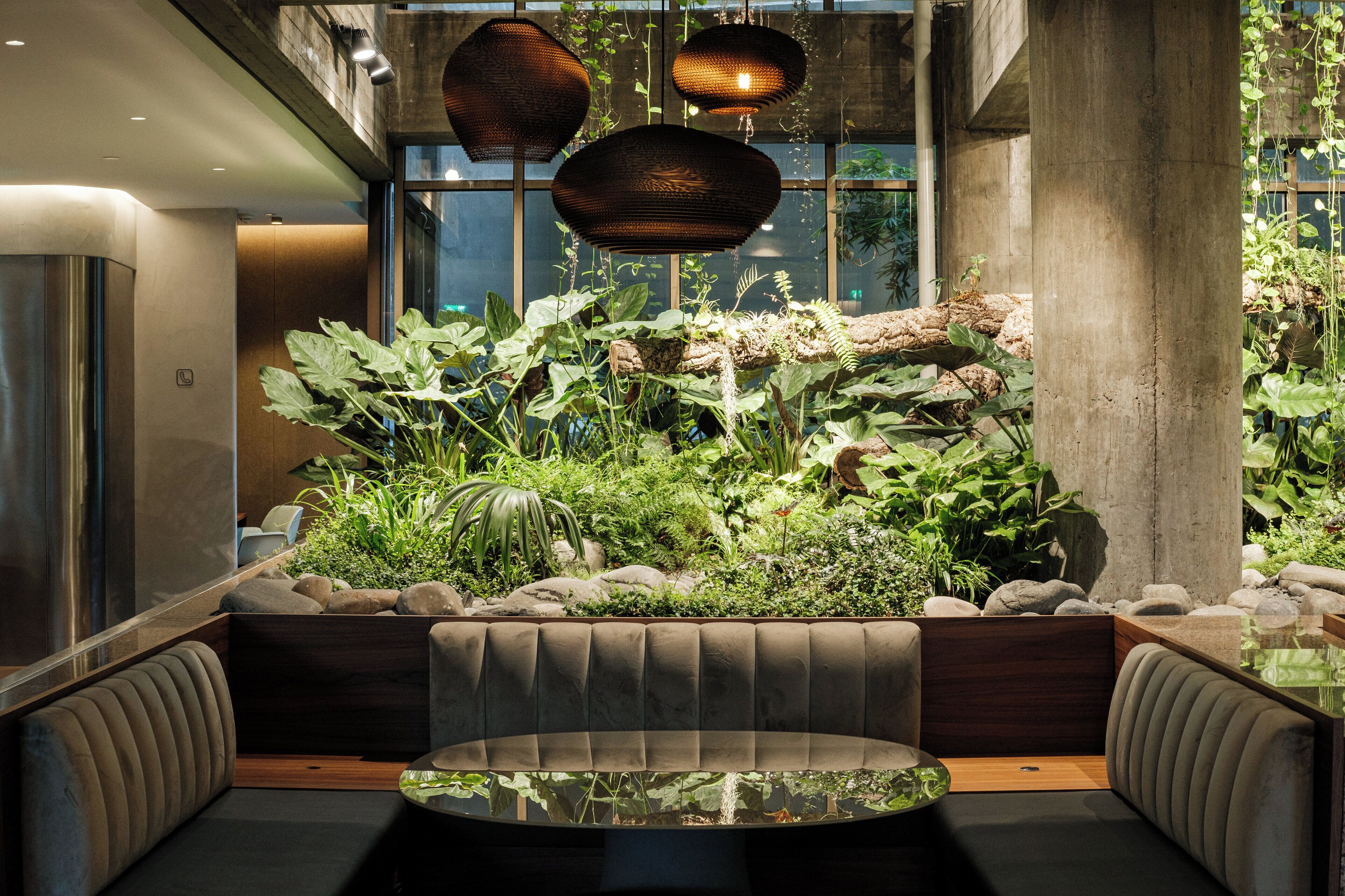 Un interior moderno con una zona de estar rodeada de abundante vegetación y una mesa de vidrio.