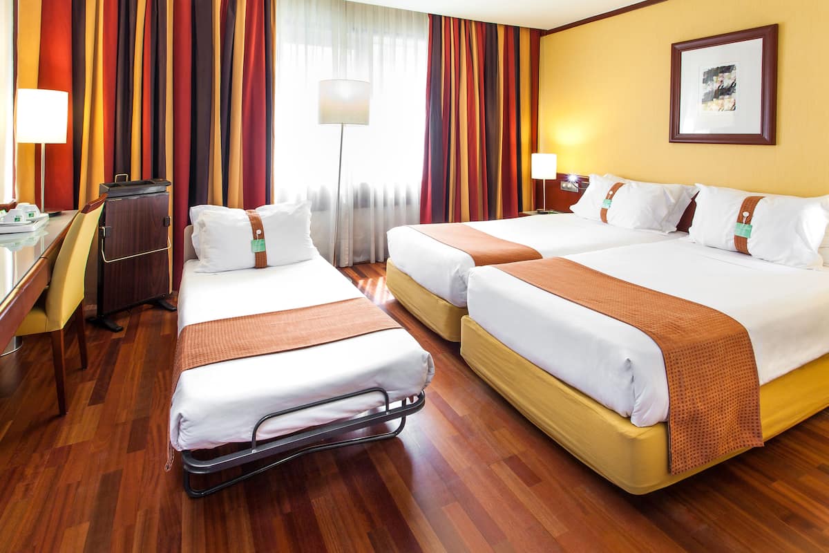 A hotel room with two beds, a desk, a chair, and a lamp.