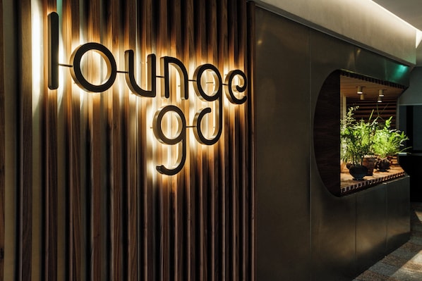 A wall with the words "lounge" illuminated in a modern font, with vertical wooden slats and a recessed area with plants. - Holiday Inn Lisbon Continental by IHG (Lisbon)