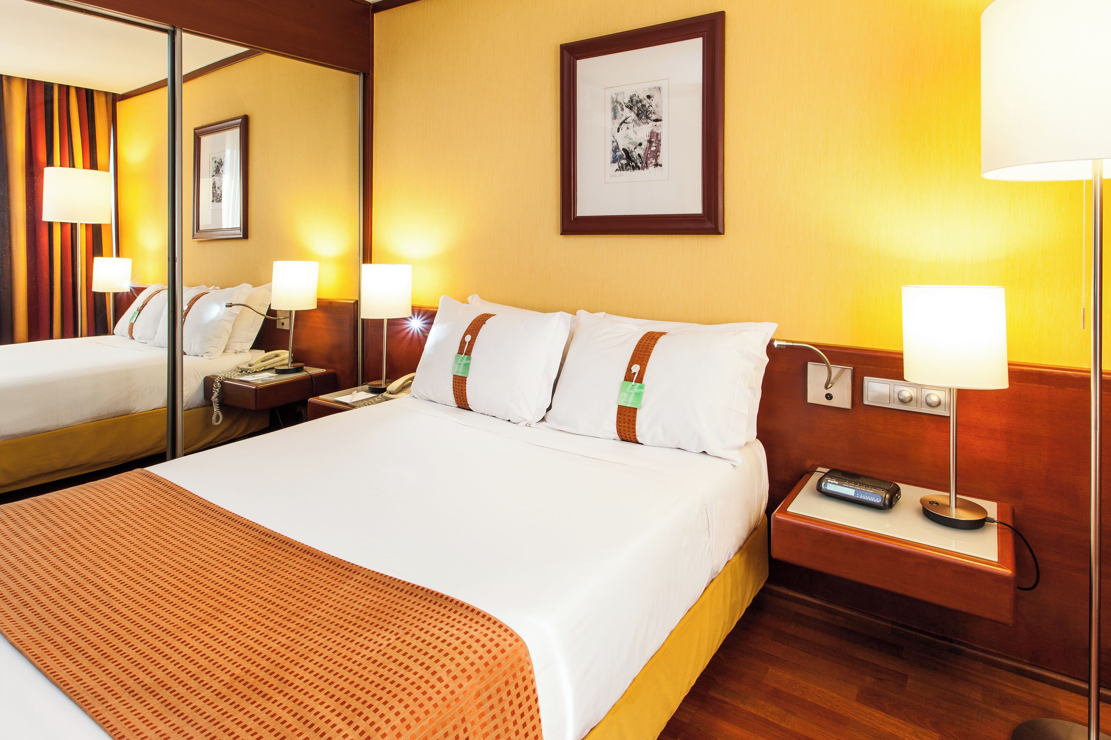 A hotel room with a large bed, bedside tables, a nightstand, a lamp, and a framed picture on the wall.