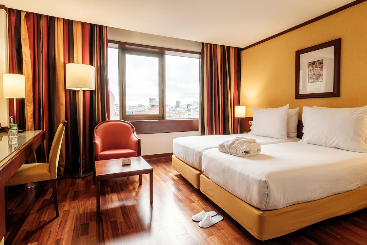 A hotel room with a bed, a desk, a chair, and a window with a city view.