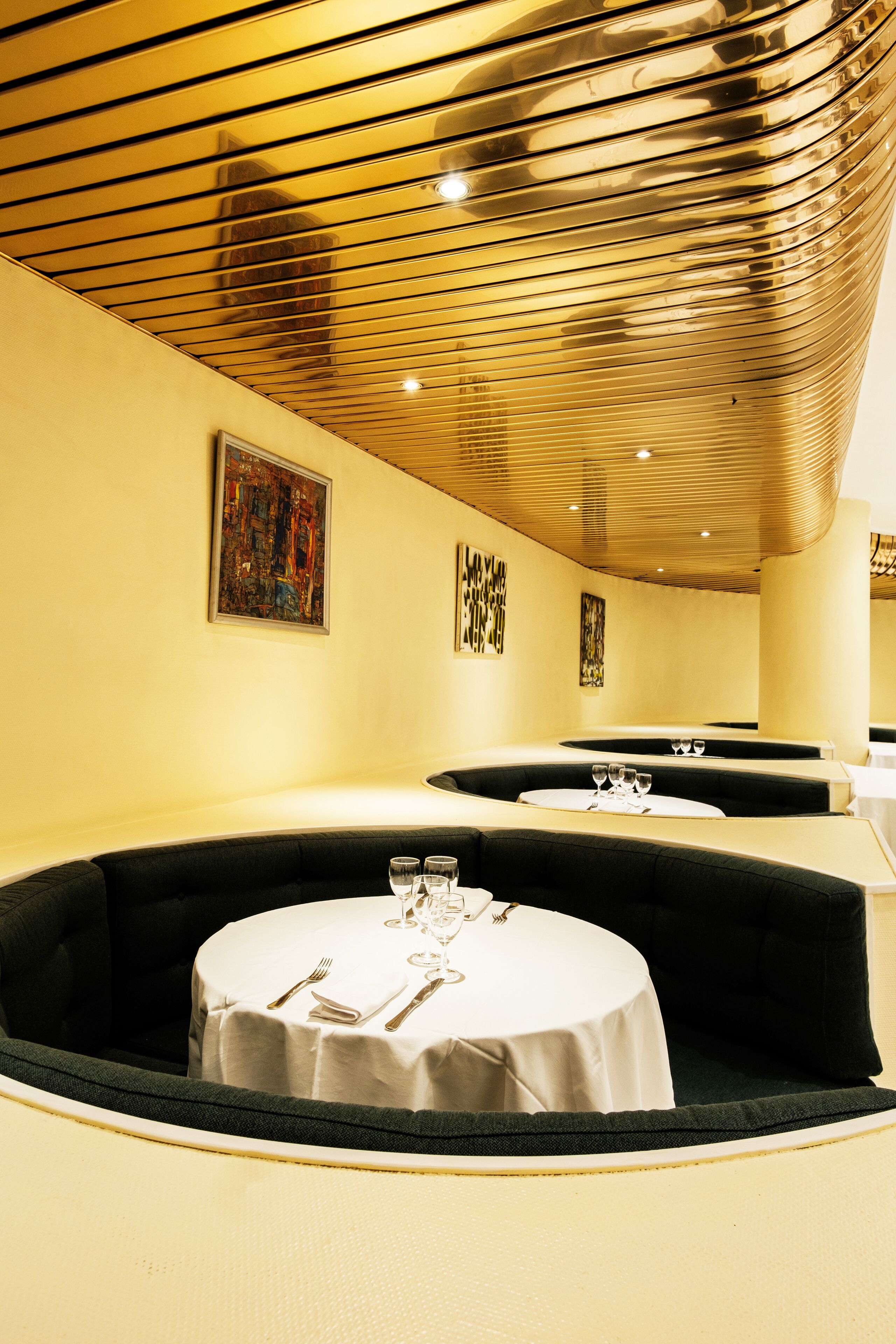 A restaurant with round tables, black cushioned seating, and artwork on the walls.