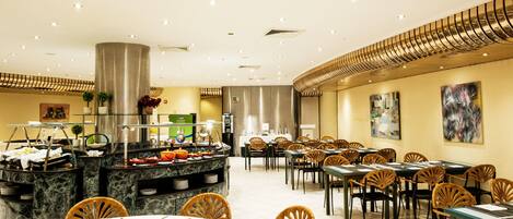 A spacious dining area with multiple tables and chairs, a buffet counter, and a modern ceiling design.