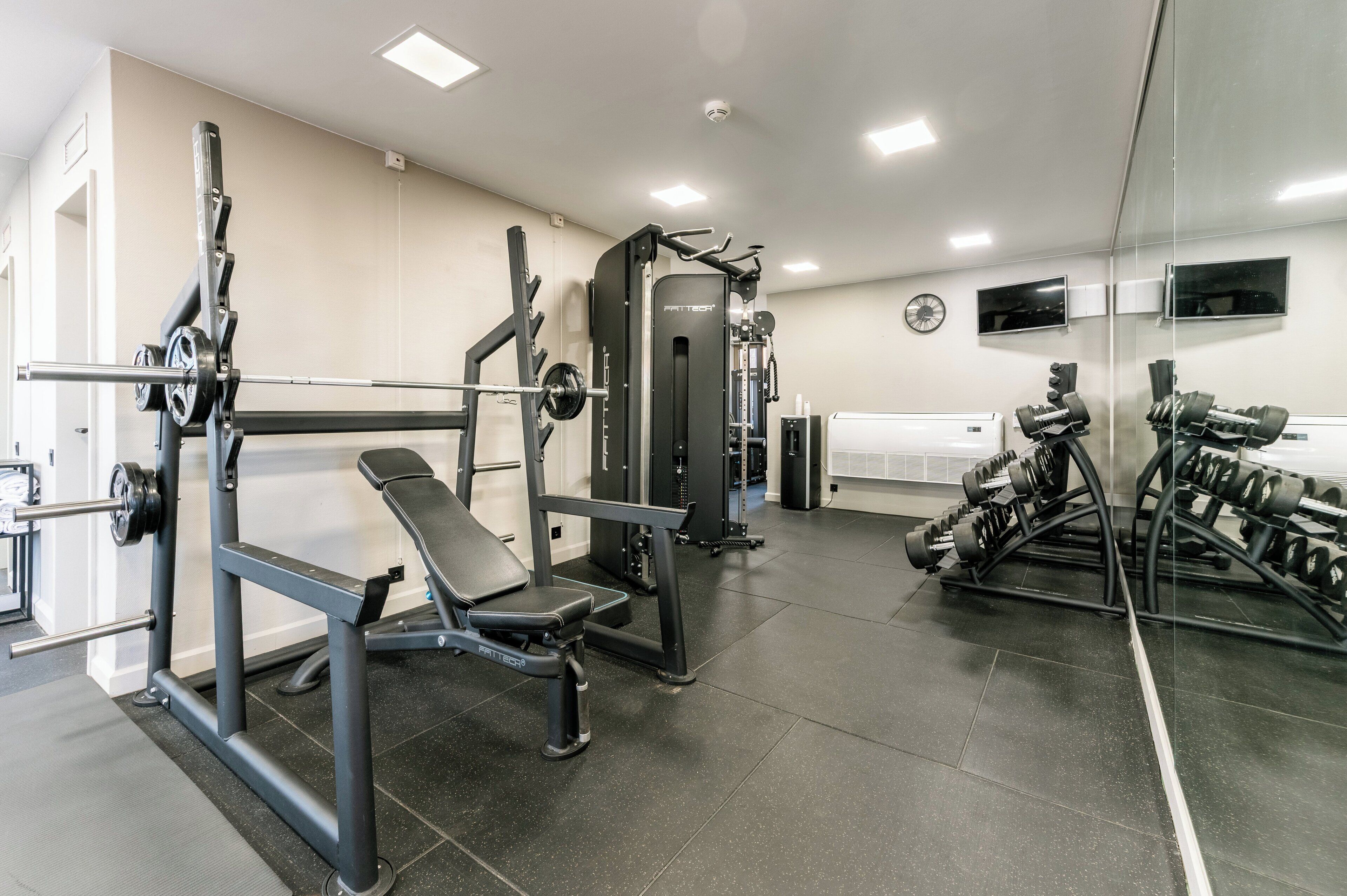 A gym with weightlifting equipment, a bench, and a mirrored wall.