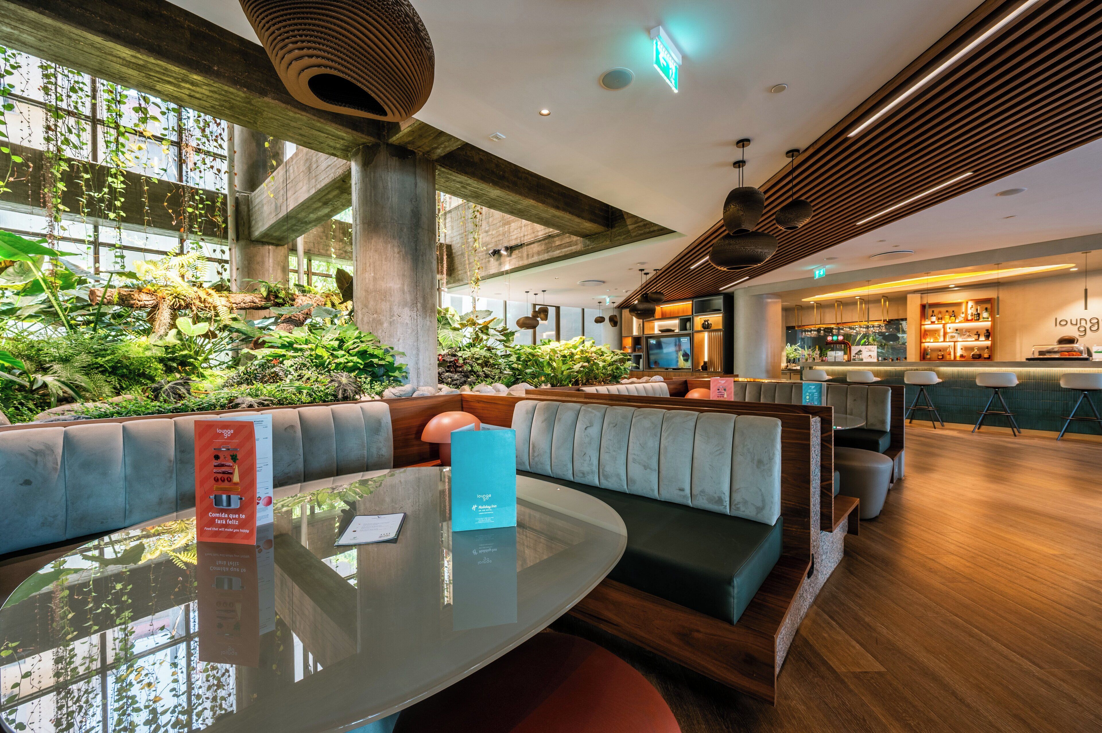 A modern lounge area with a glass table, cushioned seating, and a green wall with plants.