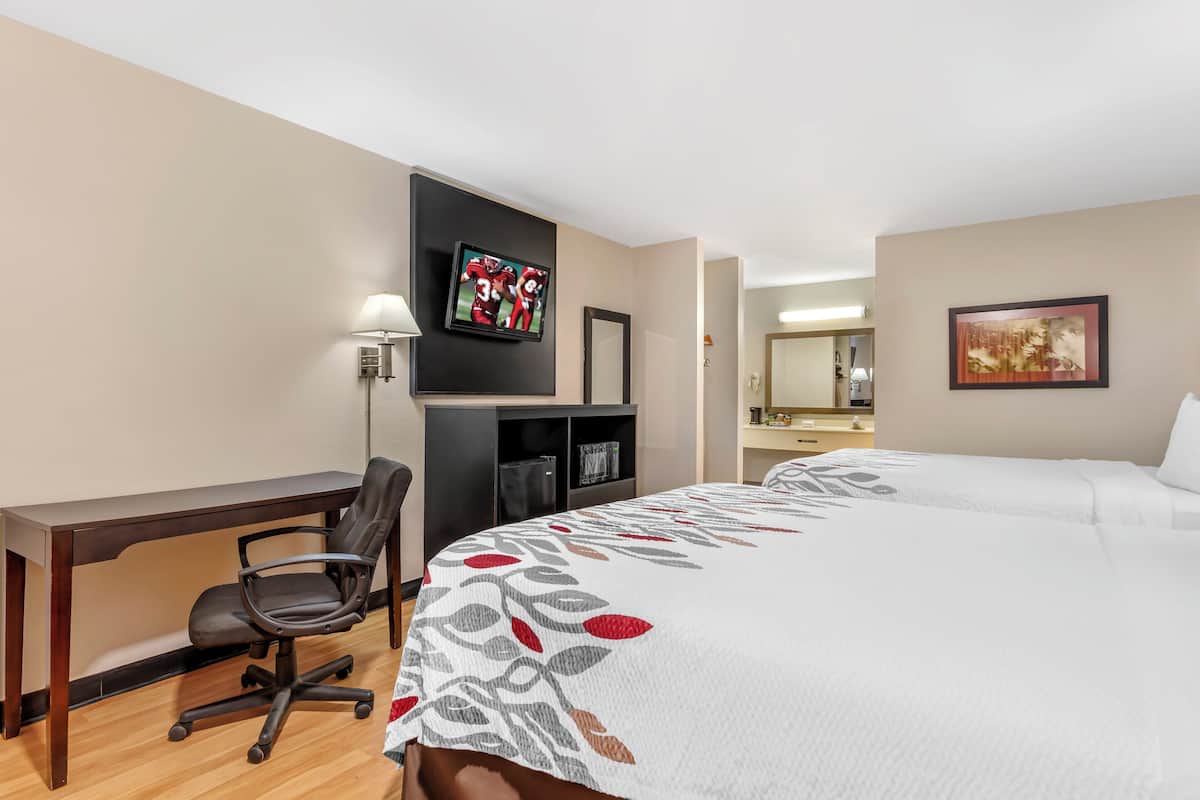 Ett hotellrum med en säng, ett skrivbord, en stol, en tv, en spegel och en tavla på väggen.