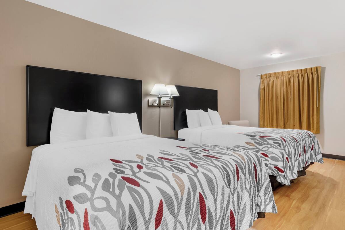 Ett hotellrum med två sängar, ett nattduksbord med en lampa och ett fönster med gardiner.