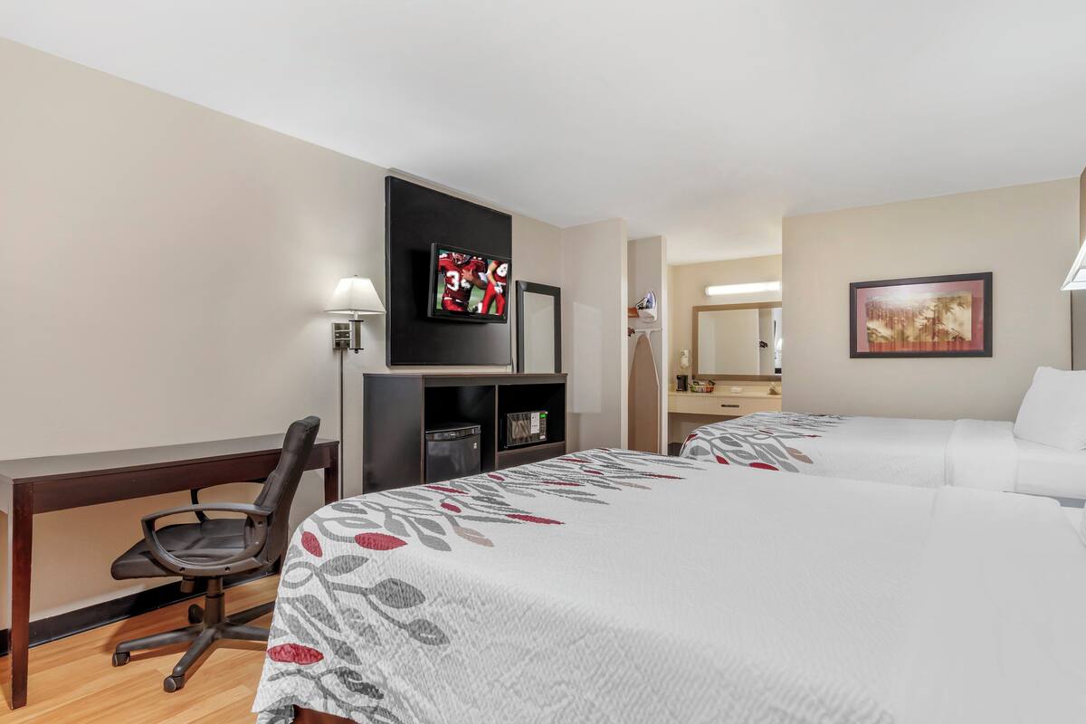 Habitación de hotel con dos camas, un escritorio con silla, televisor y un cuadro en la pared.