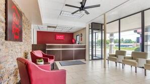 A hotel reception area with a red wall, a reception desk, and seating. - Red Roof Inn Atlanta - Kennesaw State University (Kennesaw)