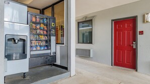 A vending machine with snacks and a water dispenser, a red door, and a building entrance. - Red Roof Inn Atlanta - Kennesaw State University (Kennesaw)
