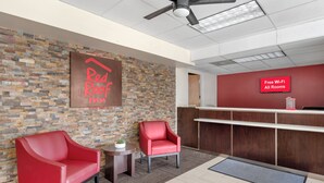L'espace d'accueil d'un hôtel Red Roof Inn, avec deux chaises rouges, un comptoir d'accueil en bois et un panneau indiquant que le Wi-Fi est gratuit dans toutes les chambres.