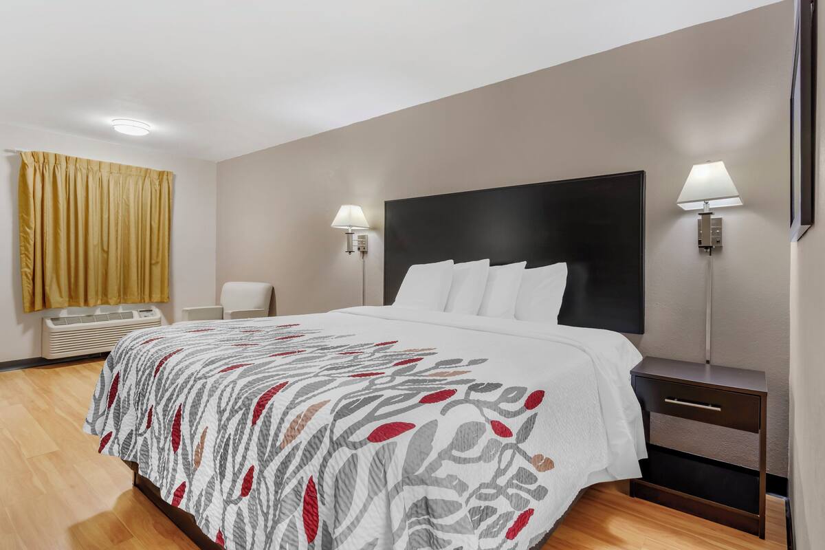 Habitación de hotel con una cama grande, dos lámparas de noche, una mesita de noche y un ventanal con cortinas.