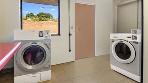 Une buanderie équipée de deux machines à laver Wascomat, une fenêtre donnant sur un paysage aride et une porte.