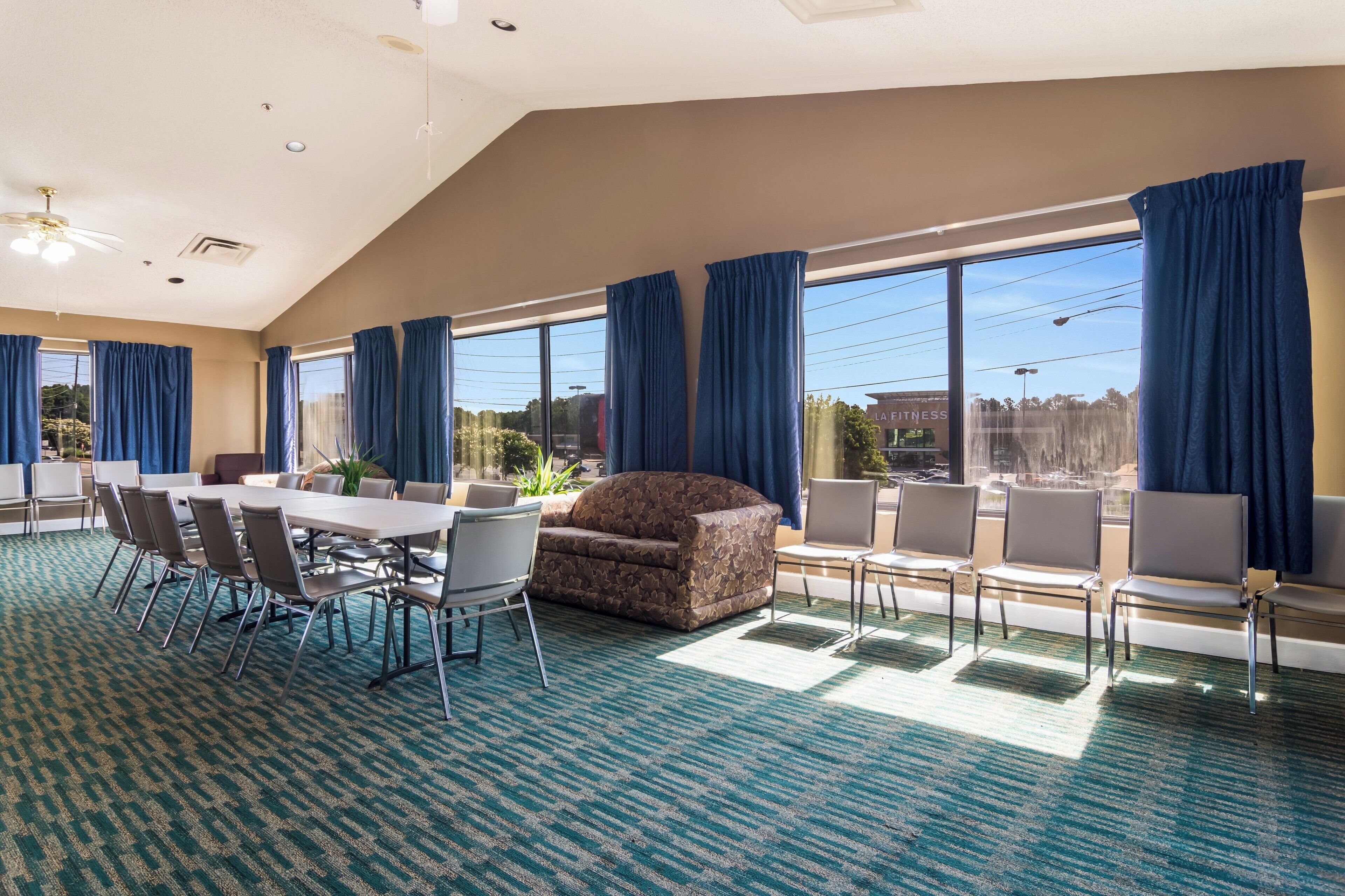 A spacious room with a large table and chairs, a sofa, and a view of the outdoors through large windows.