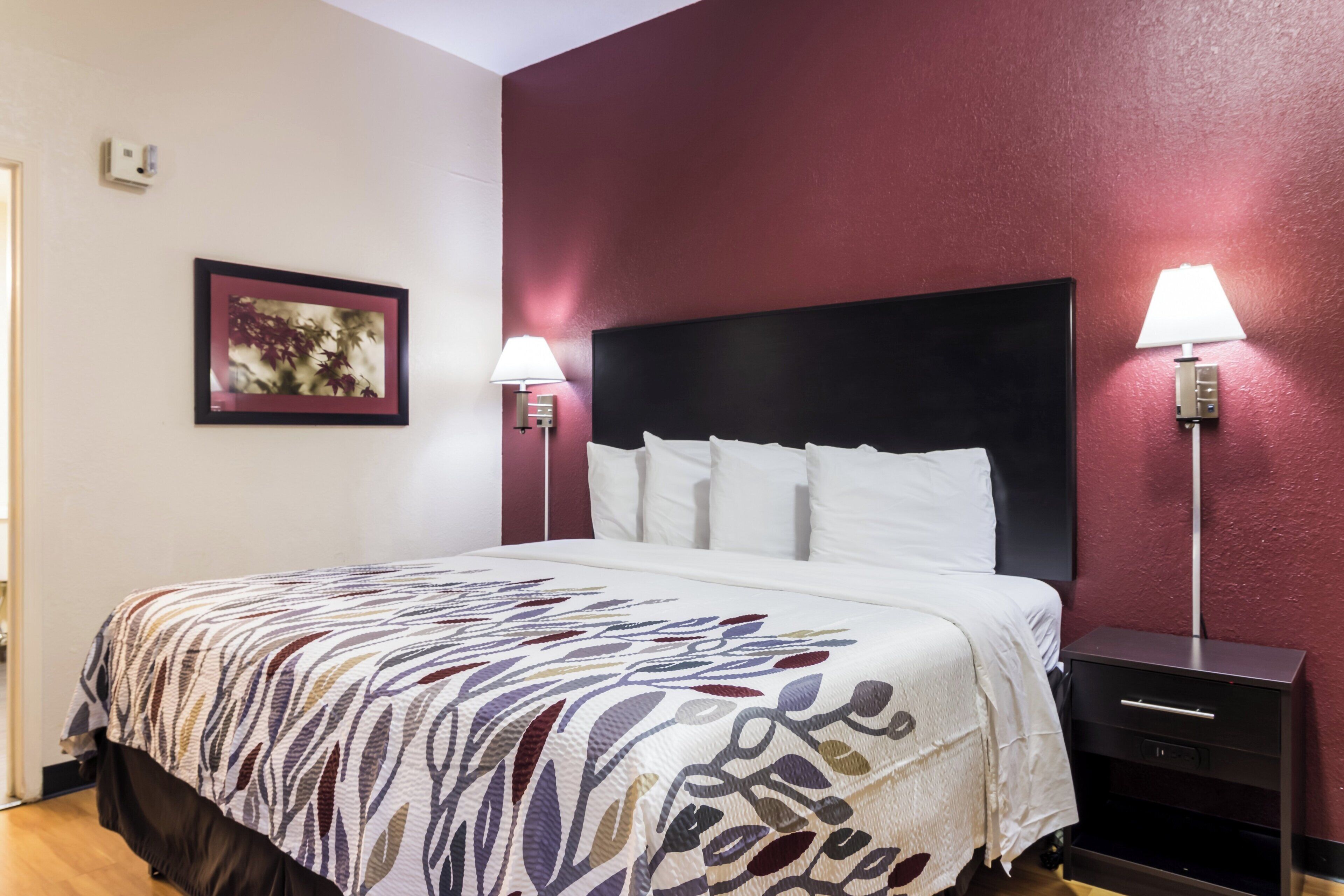 A hotel room with a bed, two bedside lamps, a nightstand, and a framed picture on the wall.
