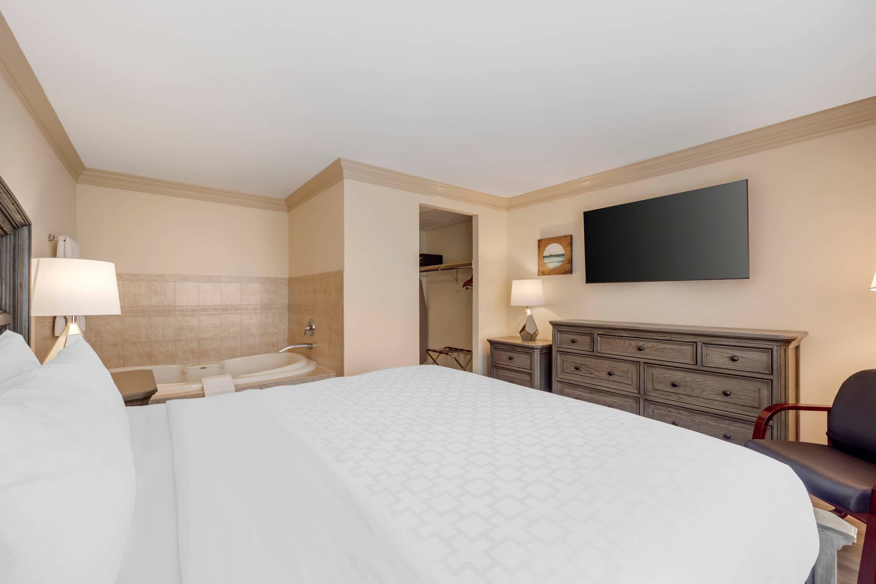 Quarto de hotel com uma cama grande, televisão de tela plana, cômoda, cadeira, escrivaninha e closet espaçoso.