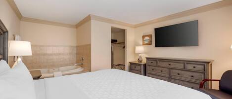 Quarto de hotel com uma cama grande, televisão de tela plana, cômoda, cadeira, escrivaninha e closet espaçoso.