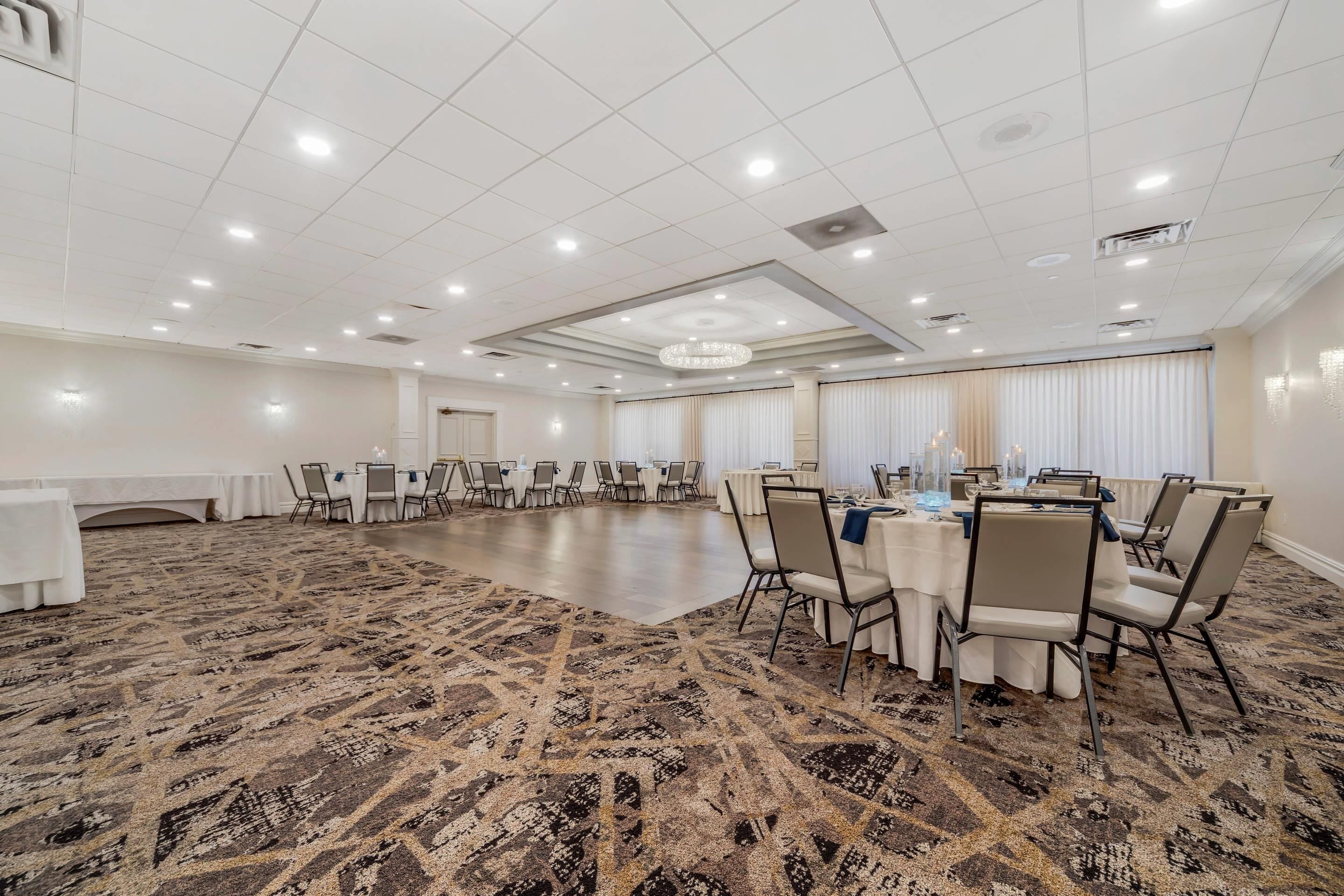 Een ruime congreszaal met een kamerbreed tapijt, ronde tafels met stoelen en een kroonluchter.