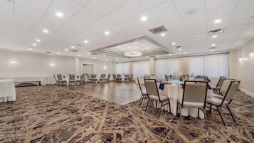 Un amplio salón de conferencias con alfombra estampada, mesas redondas con sillas y un candelabro.