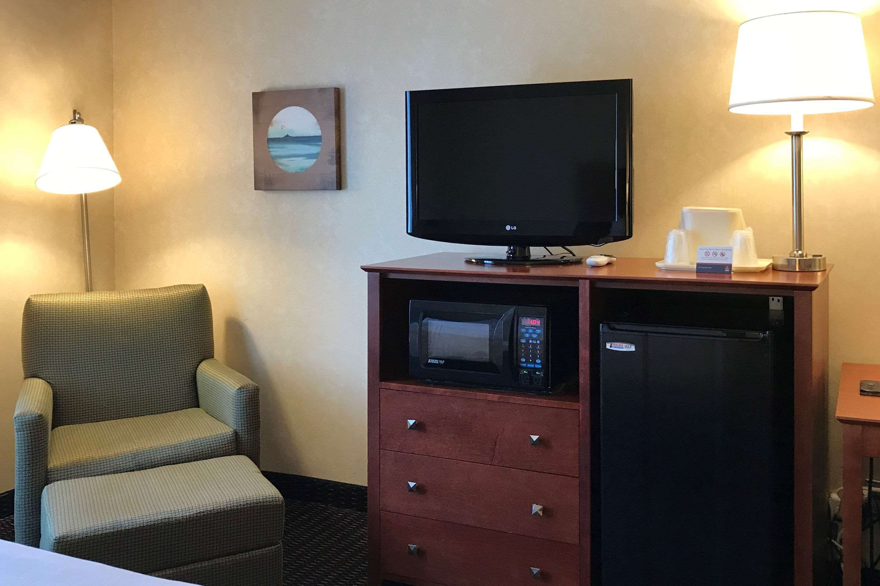 Hotelkamer met flatscreen televisie, magnetron, koelkast, stoel en tafel met lamp.