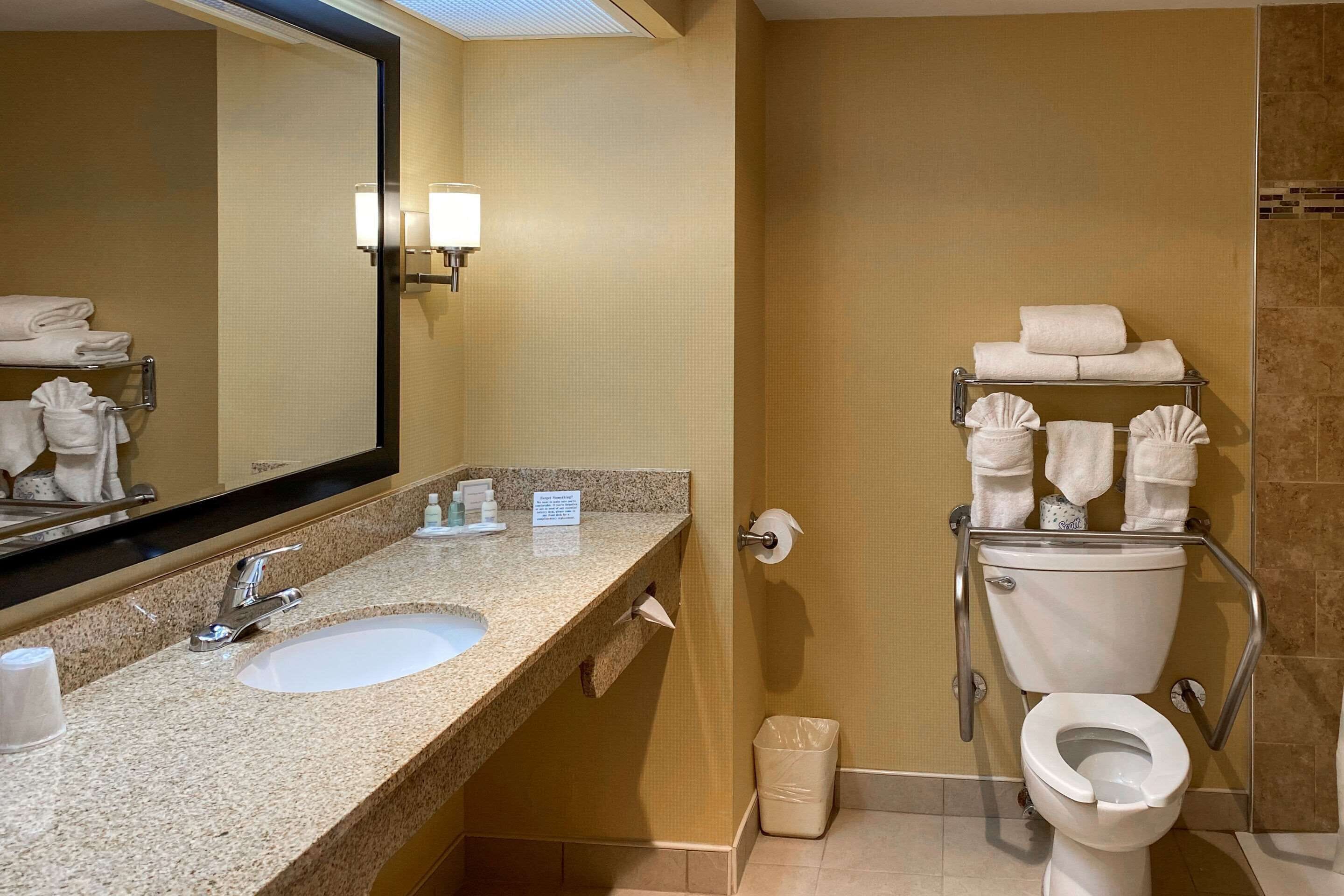 Ein Badezimmer mit Waschbecken, Spiegel, Handtuchhalter, Toilette und Handtrockner.